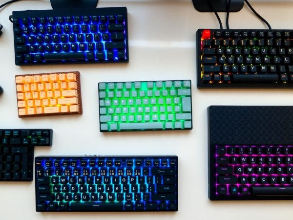 Tastaturi mecanice diverse, iluminate, cu taste colorate, aranjate estetic pe birou.